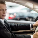 Driver in a suit at the wheel, looking back at the passenger